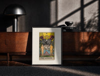 Black-framed The Lovers tarot card print on a moody console with designer coffee-table books