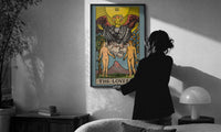 The Lovers print in a slim black frame being hung on a sunlit wall in a monochrome room