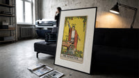 Robed magician raising a wand print in a slim black frame leaning on a dark sofa in a concrete print studio