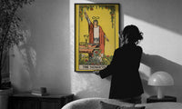 The Magician print in a slim black frame being hung on a sunlit wall in a monochrome room