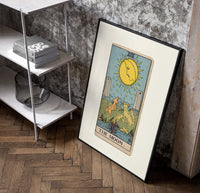 The Moon tarot card poster in a black frame leaning beside a shelf in a raw-plaster loft