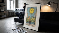 The Moon tarot card print in a slim black frame leaning on a dark sofa in a concrete print studio