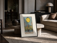 The Moon tarot card print in a black frame leaning on a travertine table in a sunlit lounge