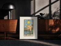 Black-framed The Star tarot card figure print on a moody console with designer coffee-table books