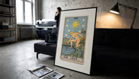 The Star tarot card figure print in a slim black frame leaning on a dark sofa in a concrete print studio