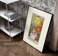 Child on white horse tarot poster in a black frame leaning beside a shelf in a raw-plaster loft