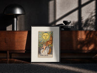 Black-framed Child on white horse tarot print on a moody console with designer coffee-table books