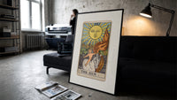 Child on white horse tarot print in a slim black frame leaning on a dark sofa in a concrete print studio