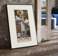The Tower tarot card print in a black frame leaning beside a vintage door on parquet