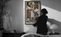 The Tower print in a slim black frame being hung on a sunlit wall in a monochrome room