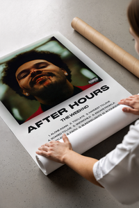 Hands unrolling the After Hours poster showing the artist face and track listings on concrete