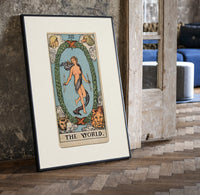 The World tarot card figure print in a black frame leaning beside a vintage door on parquet
