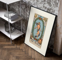 The World tarot card figure poster in a black frame leaning beside a shelf in a raw-plaster loft