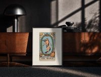 Black-framed The World tarot card figure print on a moody console with designer coffee-table books