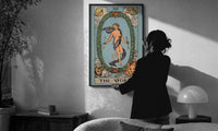 The World print in a slim black frame being hung on a sunlit wall in a monochrome room