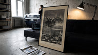 Santa Claus in reindeer sleigh over rooftops print in a slim black frame leaning on a dark sofa in a concrete print studio