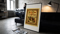 Santa Claus sewing doll clothes in workshop print in a slim black frame leaning on a dark sofa in a concrete print studio