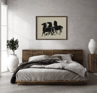 Three black horses standing print in a dark wood frame above a rattan bed on a plaster wall