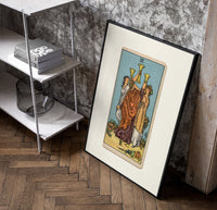 Three women toasting golden cups poster in a black frame leaning beside a shelf in a raw-plaster loft