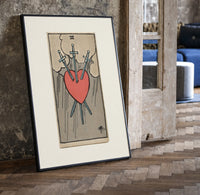 Heart pierced by three swords print in a black frame leaning beside a vintage door on parquet