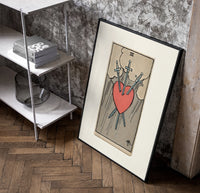 Heart pierced by three swords poster in a black frame leaning beside a shelf in a raw-plaster loft
