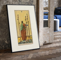 Figure holding staffs facing sea print in a black frame leaning beside a vintage door on parquet