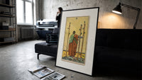 Figure holding staffs facing sea print in a slim black frame leaning on a dark sofa in a concrete print studio