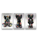 Three-panel KAWS graffiti triptych showing sitting and standing companions covered in colorful tags and paint splatters