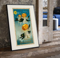 Black cats with jack-o-lantern heads print in a black frame leaning beside a vintage door on parquet