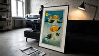 Black cats with jack-o-lantern heads print in a slim black frame leaning on a dark sofa in a concrete print studio