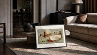 Children ice fishing beside an ice boat print in a slim black frame leaning on a travertine coffee table