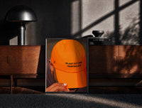Black-framed Trusting God Orange Cap print on the floor in front of a dark wooden console