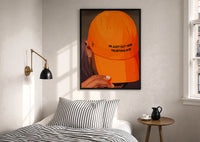 Trusting God Orange Cap print in a black frame above a bed with striped linens, a brass wall lamp and a sunlit window
