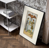 Two people toasting golden cups poster in a black frame leaning beside a shelf in a raw-plaster loft