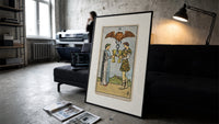 Two people toasting golden cups print in a slim black frame leaning on a dark sofa in a concrete print studio