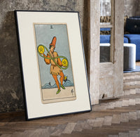Two of Pentacles tarot figure print in a black frame leaning beside a vintage door on parquet