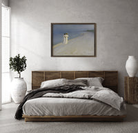 Two women walking on beach print in a dark wood frame above a rattan bed on a plaster wall