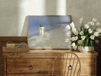 Two women walking on beach print in an oak frame on a farmhouse dresser beside white tulips