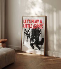 Unframed fashion poster leaning on cream wall in warm room with herringbone floor and round wooden side table