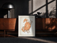 Black-framed Cancer crab zodiac constellation illustration print on a moody console with designer coffee-table books