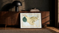 Capricornus sea-goat constellation figure print in a black frame leaning against a walnut console in lamplight