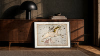 Unicorn and dog constellation illustration print in a black frame leaning against a walnut console in lamplight