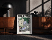 Black-framed Vintage Macintosh computer with plants print on a moody console with designer coffee-table books