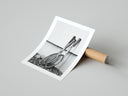 Black and white vintage wooden tennis rackets poster partially unrolled next to a cardboard shipping tube on gray.