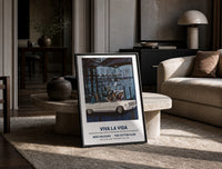 White convertible car with elegant couples print in a black frame leaning on a travertine table in a sunlit lounge