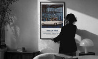 White convertible car with elegant couples print in a slim black frame being hung on a sunlit wall in a monochrome room