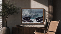 Crashing waves on rocky coast print in a wood frame above a fluted sideboard beside an olive tree