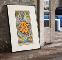 Wheel of Fortune tarot card print in a black frame leaning beside a vintage door on parquet