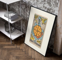 Wheel of Fortune tarot card poster in a black frame leaning beside a shelf in a raw-plaster loft