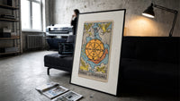 Wheel of Fortune tarot card print in a slim black frame leaning on a dark sofa in a concrete print studio
